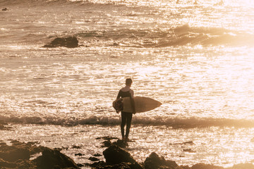 Fototapeta na wymiar Surfer on the ground walking to the ocean waves to start surfing activity. Sport and outdoor lifestyle for young people enjoy the nature and have fun. Vacation and alternative life concept