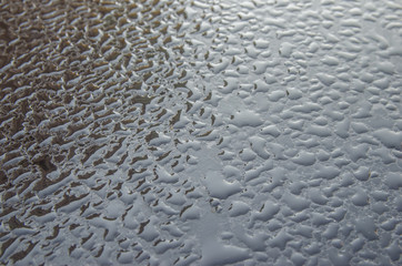 drops of rain on the hood of a black car with a reflection of the sky