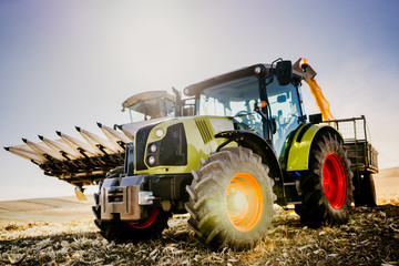 Agriculture industry machinery. Combine harvester and tractor with trailer unloading harvest. Farmer working details