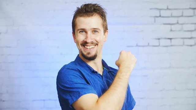 Fuck yea pose with arm 4K. Static portrait shot of a man in focus happy holding up an arm. Background bricked wall out of focus.
