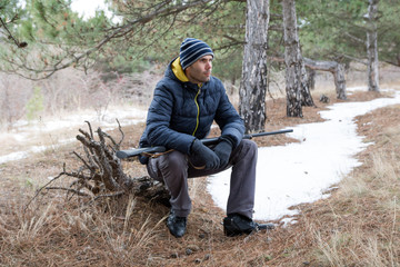 caucasian man is sittting in winter forest with a shotgun. Hunting with a shotgun