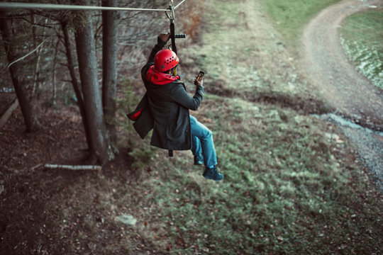A young man takes a photo while zip lining in the woods in upstate New York