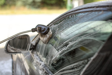Side of a car washed in self serve carwash. Brush cleaning glass, strokes visible in shampoo foam.