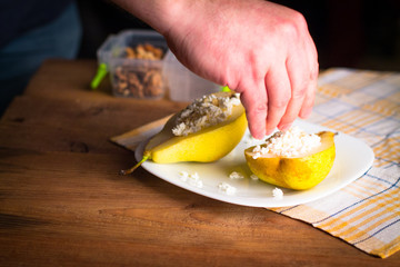 Backstage with a shot of a pear with cottage cheese, nuts, cinnamon and honey on a wooden, subject table. The hands of the photographer in the frame. Creating a photo