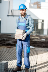 Obraz premium Porait of a builder in uniform holding paving tiles on the construction site with white houses on the background