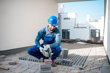 Builder in uniform cutting paving tiles with electric cutter on the construction site with white...