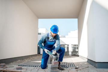 Builder in uniform cutting paving tiles with electric cutter on the construction site with white...