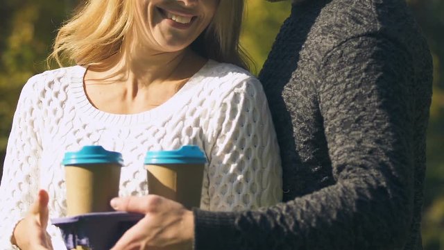Guy giving cup of hot drink to girl outdoor, coworkers warming at coffee break