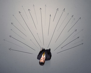 Young contemplating businessman stands in front of grey arrows 