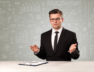 Young handsome businessman sitting at a desk with white graphs and calculations behind him 