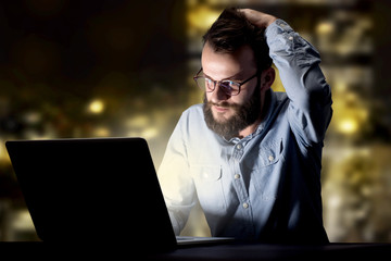 Young handsome businessman working late at night in the office with city lights in the background