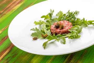 Beef tartare with capers on a green wooden table