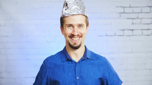 The tin-foil hat person mocking the stereotypes meme 4K. Static portrait shot of a man in focus wearing a blue elegant shirt. Shoot on the bricked wall background with blue light.