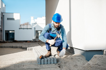 Builder in uniform mounting paving tiles hammering a pile on the construction site outdoors