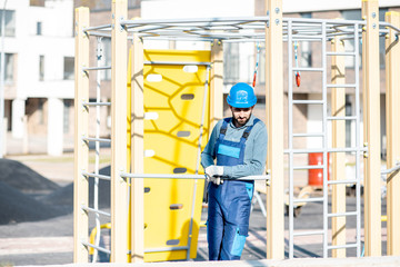 Handsome workman in uniform mounting ladder for kids playing on the playground outdoors