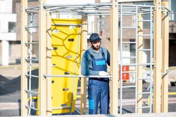 Handsome workman in uniform mounting ladder for kids playing on the playground outdoors