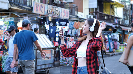 Fototapeta premium Beautiful young woman caucasian listening to music and walking street in evening at Bangkok, Thailand.