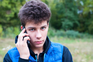 Guy in a blue jacket in the park while walking talking on the phone with his parents - listening carefully to their guides