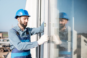Workman in uniform mounting windows checking the level on the white building facade