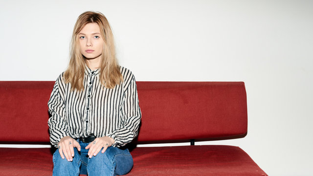 Emotionless young woman on red sofa