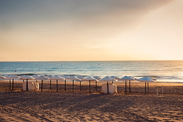 Obraz premium sunrise in secluded beach with white umbrellas. Alicante, Spain