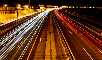 Fototapeta na wymiar DIFFERENT WHITE, BLUE AND RED LIGHTS OF MANY VEHICLES DRIVING IN A CURVE OF A SPANISH MOTORWAY WITH THE LIGHT OF A CITY AT THE END OF THE HORIZON