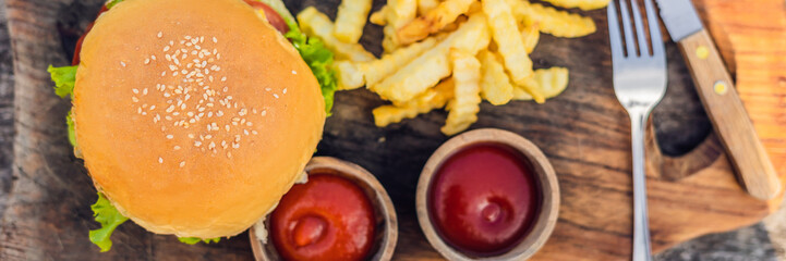 Closeup of fresh burger with French fries on wooden table with bowls of tomato sauce. lifestyle food BANNER, LONG FORMAT