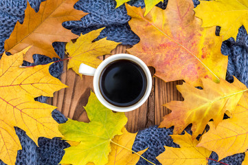 Cup of coffee with autumn leaves and knitted scarf on wooden background. Top view.