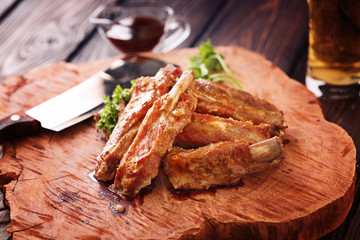 Roasted spare ribs on a wooden board with meat hatchet, BBQ sauce and glass of beer on a rustic wooden table