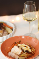 Plate with pork belly roast, mashed potatoes and roasted vegetables. Glass of white wine in the background. Served on a holiday table. Selective focus.