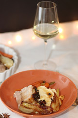 Plate with pork belly roast, mashed potatoes and roasted vegetables. Glass of white wine in the background. Served on a holiday table. Selective focus.