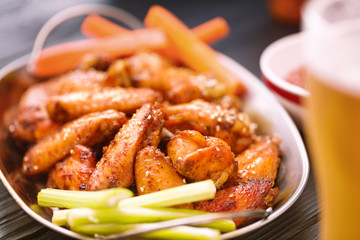 Roasted chicken wings served on a metal plate with beer, carrots and celery