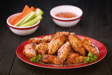 Roasted chicken wings served on a red plate with carrot, celery and sause.
