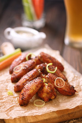 Roasted chicken wings served on a wooden board with glass of beer, carrot, celery and sause