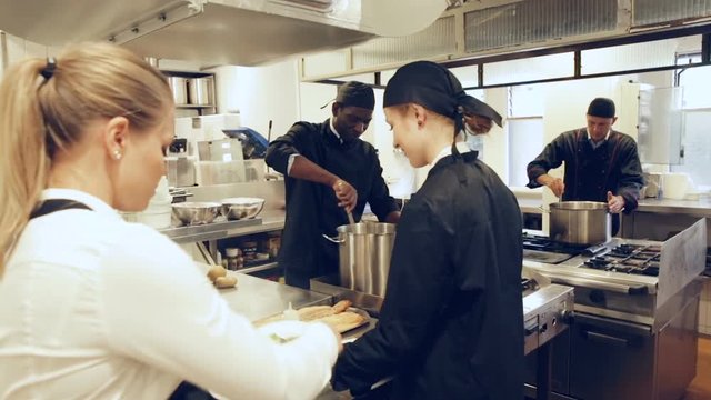 Attractive young waitress taking prepared dishes from chef in kitchen of modern restaurant 