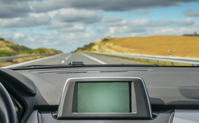 Selective focus of generic built in GPS navigator on dashboard of a car going down the scenic...