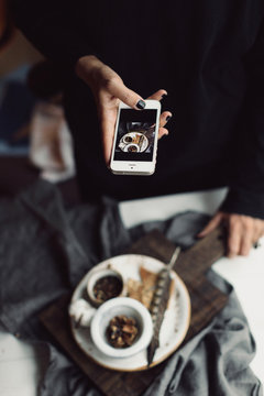 Food served on a plate with grey towel, feather and hands taking a picture with a phone
