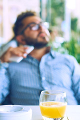 People, music, technology, leisure and lifestyle - young hipster man in glasses with earphones and smartphone on the terrace of a summer cafe in the city.