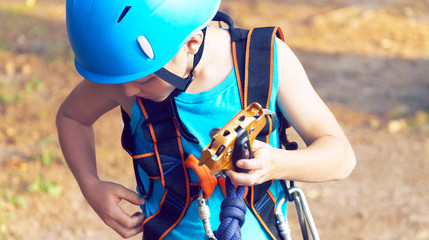 Cute little boy in blue shirt and helmet having fun at the adventure park, holding ropes and prepering to climb wooden stairs. Hobby, active lifestyle concept.