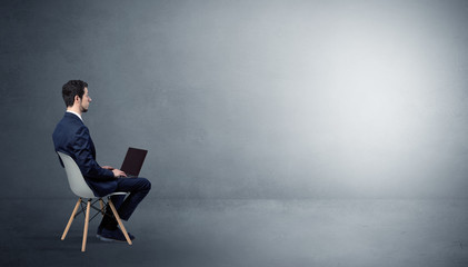 Businessman staying in an empty grey dark room with stuffs on his lap
