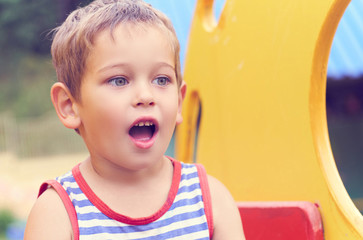 Little toddler boy in striped t-shirt having fun on playground on summer day.