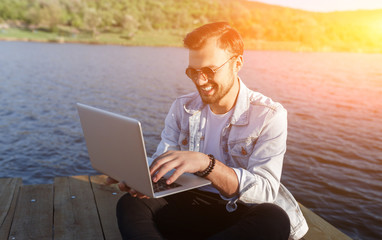 Cheerful man using laptop on pier