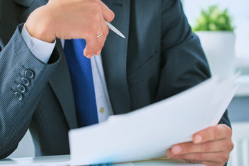 Closeup portrait of unrecognizable businessman in black formal suit reading contract documents at...