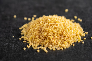 useful grits Bulgur heap on a dark, gray, stone background