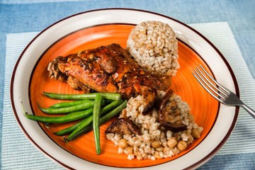 Baked rabbit thig,barley pearl and chickpeas,green bean on plate on table.
