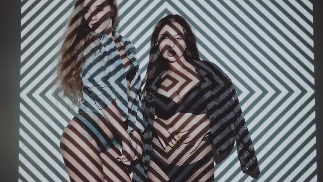 Two beautiful women in lingerie and jacket dancing with projected pattern on them. Music, nightclubs, shows and entertainment concept - video in slow motion
