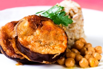 Fried breaded aubergine,chickpeas and barley pearl on white plate.