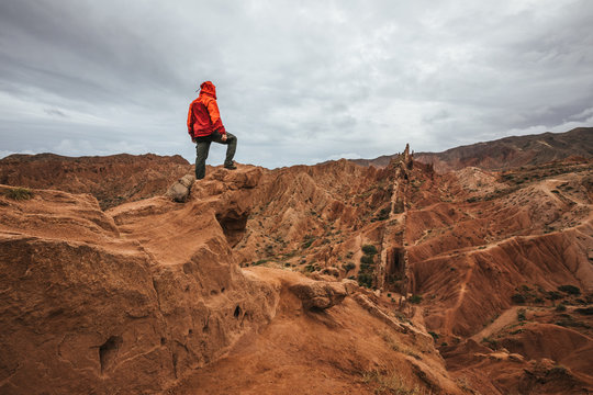 male hiker in red jacket standing on top of a bizzare rugged mountain landscape, kyrgyzstan