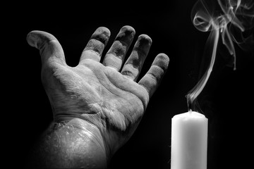 Ausgegangene Kerze mit einer flehenden Hand vor schwarzem Hintergrund