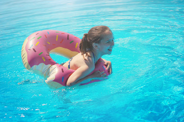 Girl teenager in a swimsuit swims with an inflatable ring in the pool with blue water.